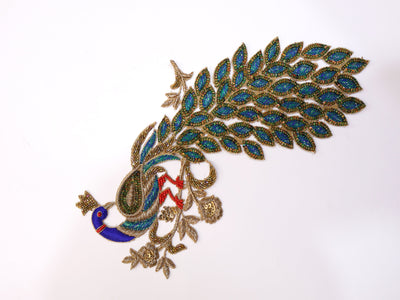 A hand embroidered sequin applique patch featuring a peacock design with blue and green sequins and red and blue embroidery.