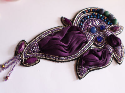 A dark purple embroidered applique patch featuring handcrafted Indian artwork with beads and pearls.