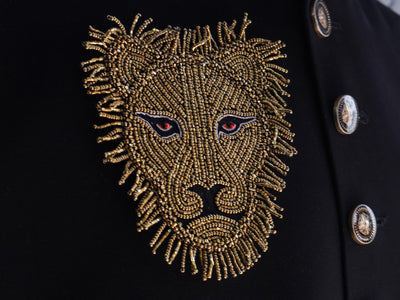 A close-up of a golden embroidered applique patch of a lion's face on a black background.